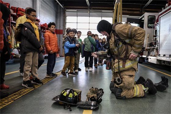 Third graders watching a fire fighter put on gear during visit to Town Hall