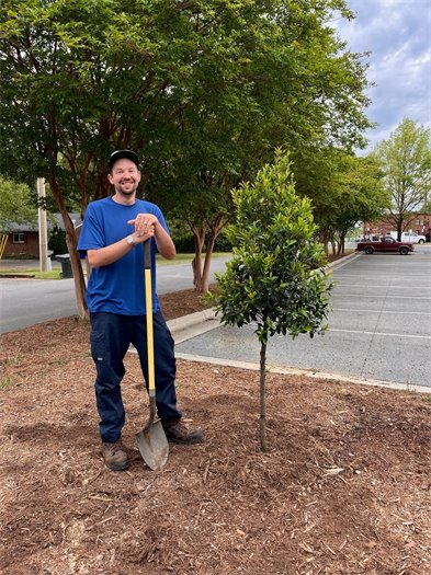 A Public Works staff member poses by a newly planted tree at Carrboro Town Hall in honor of Arbor Day 2024