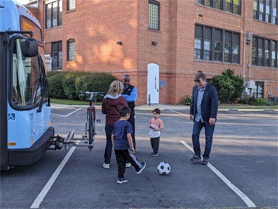 Kids and adults play with a soccer ball near a Chapel Hill Transit bus outside of Carrboro Town Hall at Earth Day